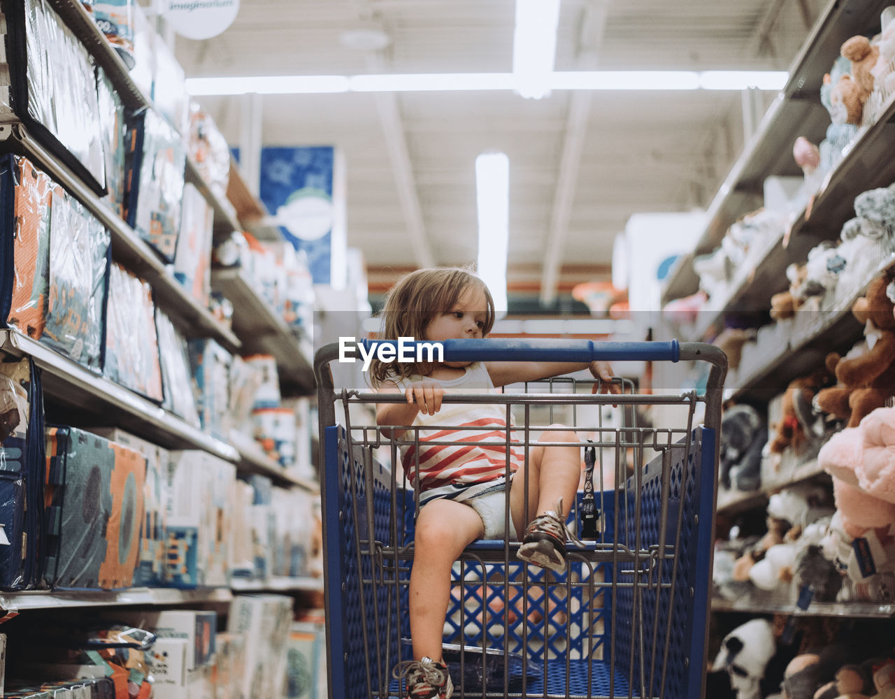 Playful girl sitting in shopping cart at supermarket