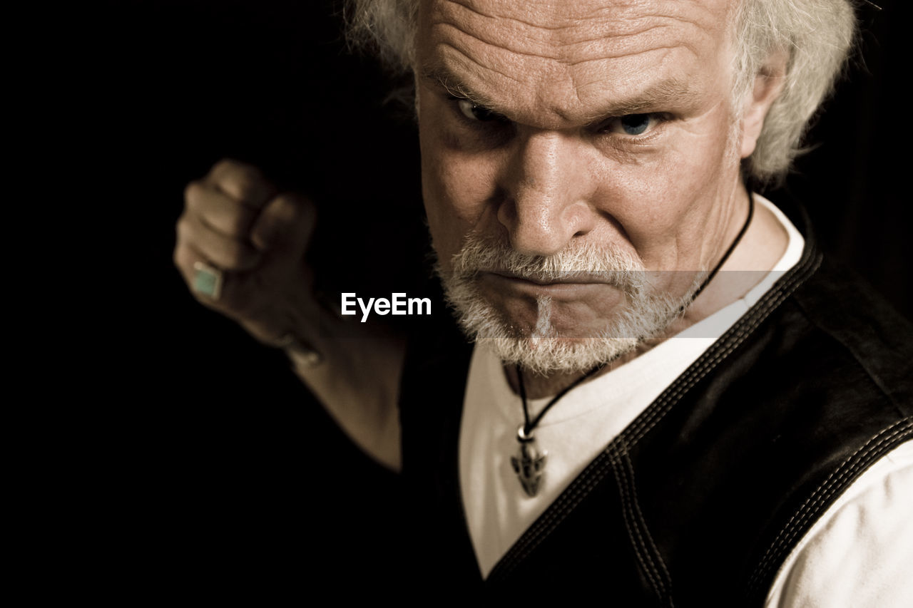 Portrait of angry senior man with clenching fist against black background