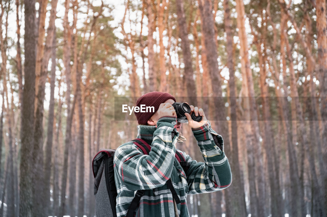 Man photographing while standing in forest during winter