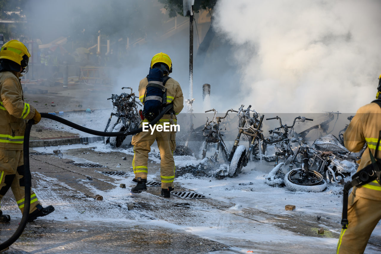 Rear view of firefighters extinguishing burning motorcycles on road in city