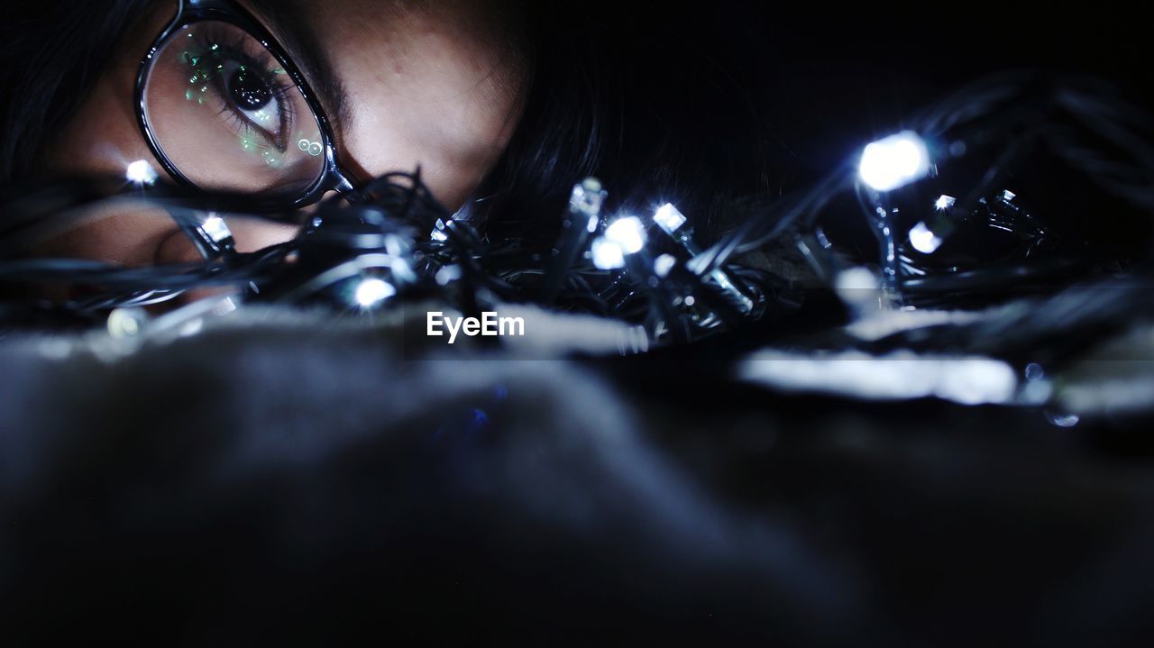 Close-up of young woman with illuminated string lights