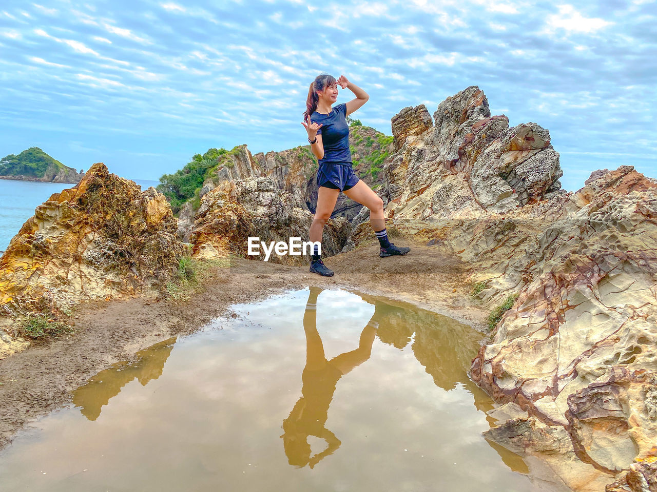 Full length of young woman standing on rock against sky