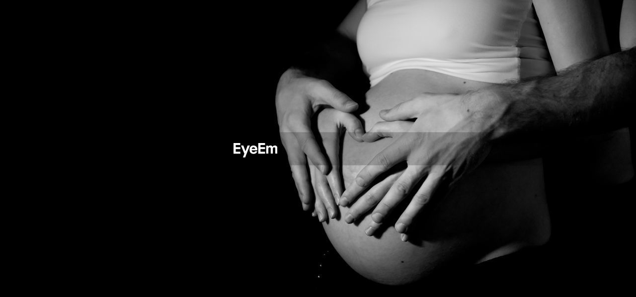 Midsection of man touching pregnant woman belly against black background
