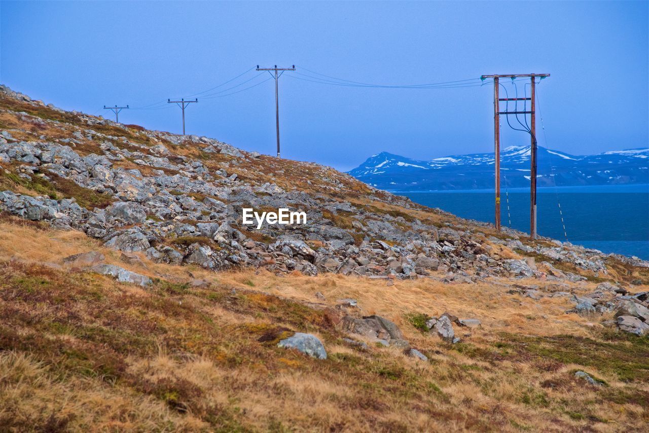 ELECTRICITY PYLONS ON MOUNTAIN AGAINST SKY