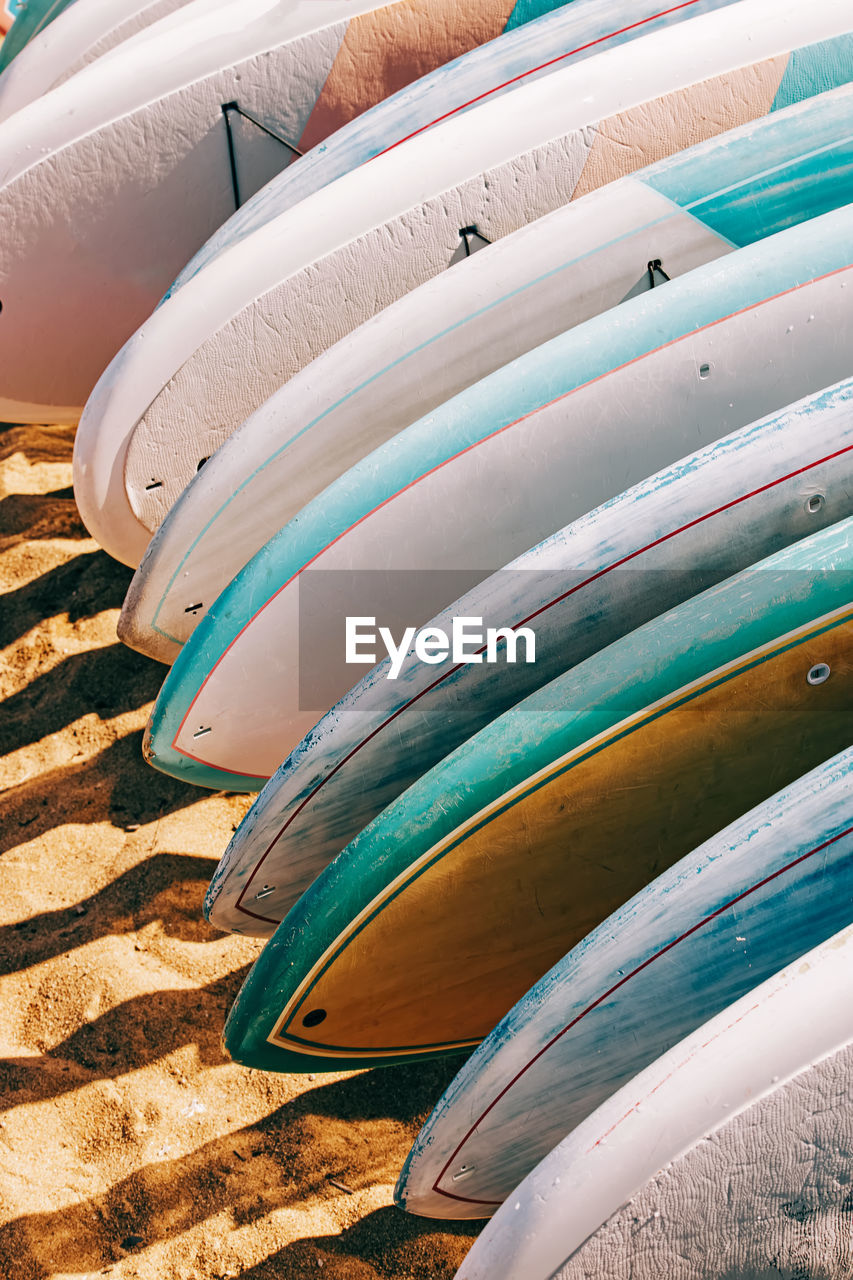 Close-up of colorful paddle boards for rent lying on the sand.