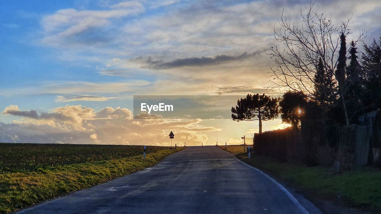 Road amidst trees on field against sky at sunset