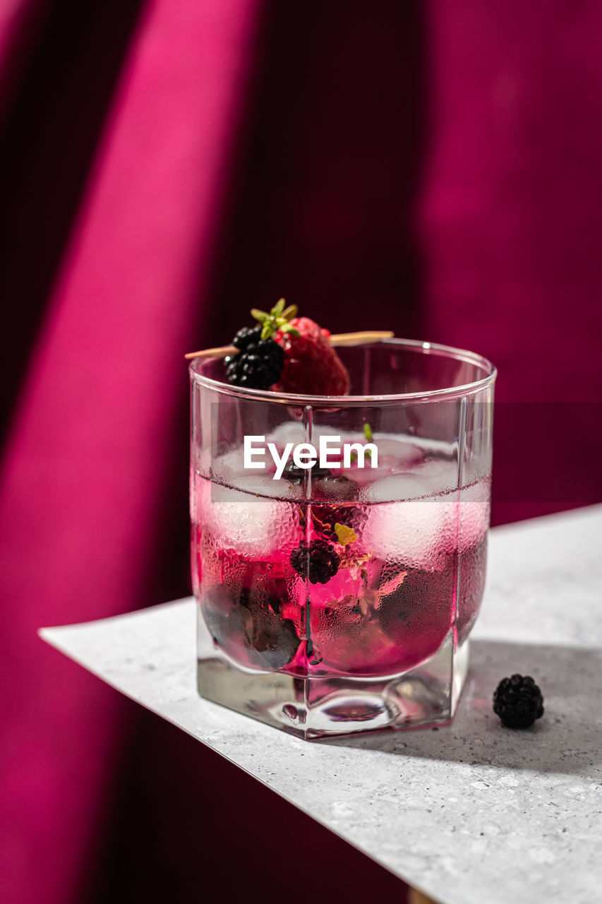 Glass of refreshing cocktail with blackberry and raspberry on wooden toothpick on table