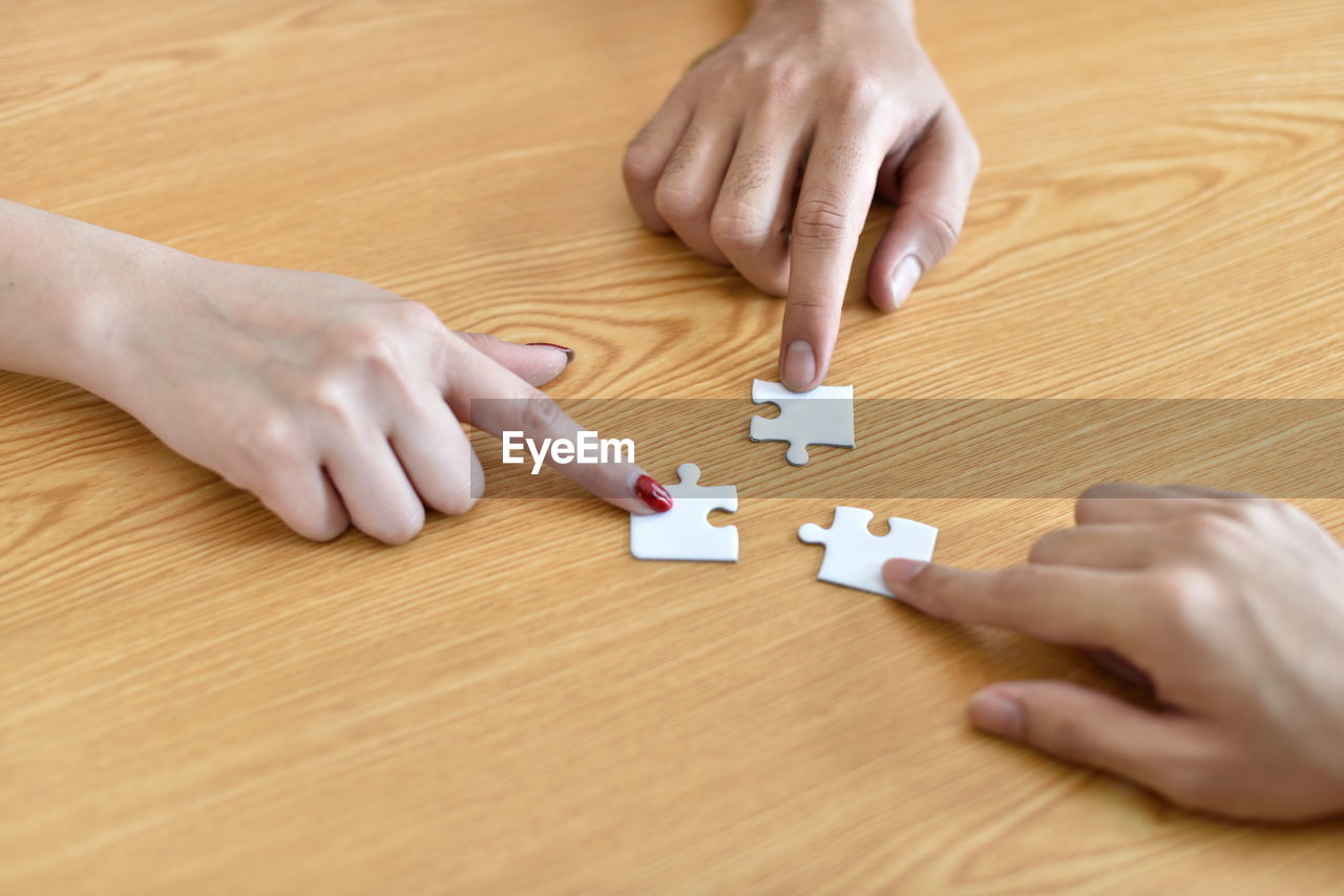 Cropped hands of people holding jigsaw pieces on table