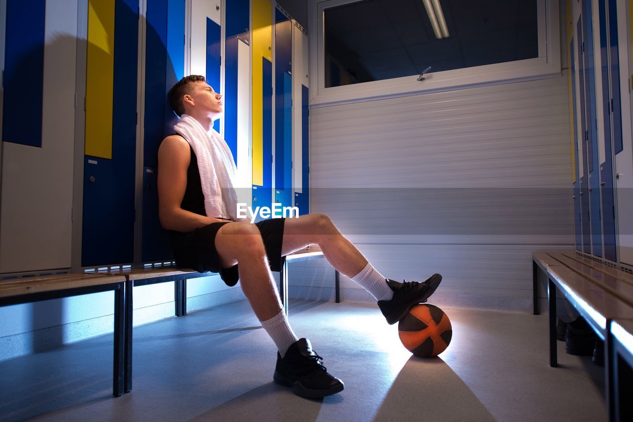 Full length of basketball player relaxing on seat in dressing room