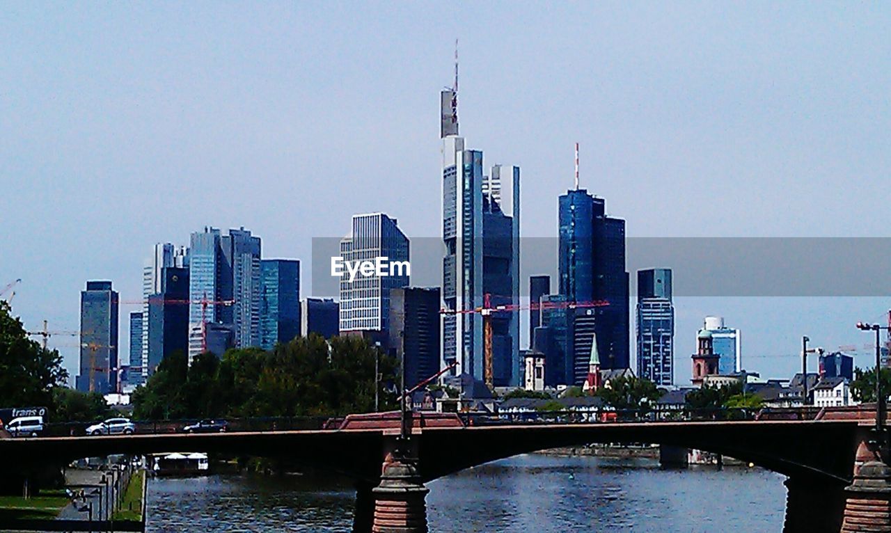 BRIDGE OVER RIVER WITH CITYSCAPE IN BACKGROUND