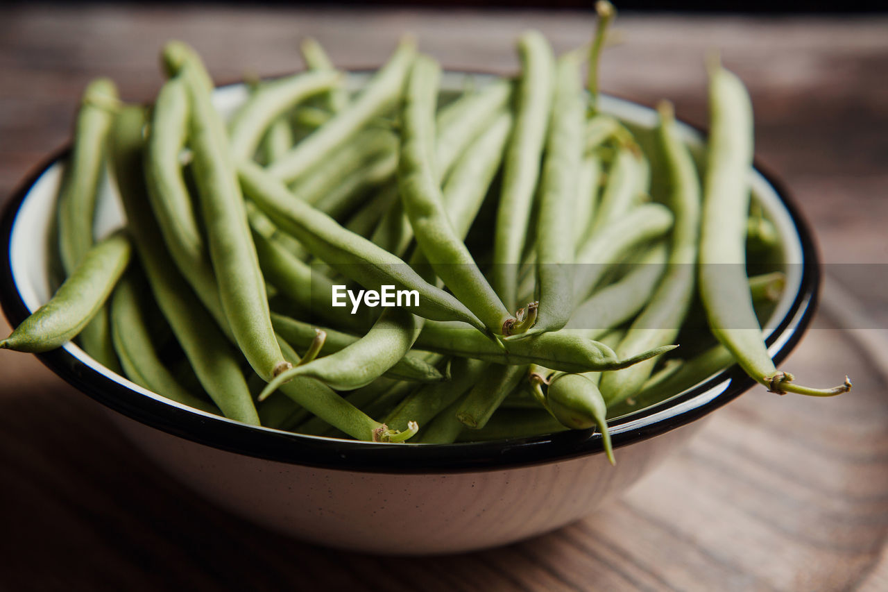 Top view of fresh whole and cut green beans in wooden and metal bowls on linen towel