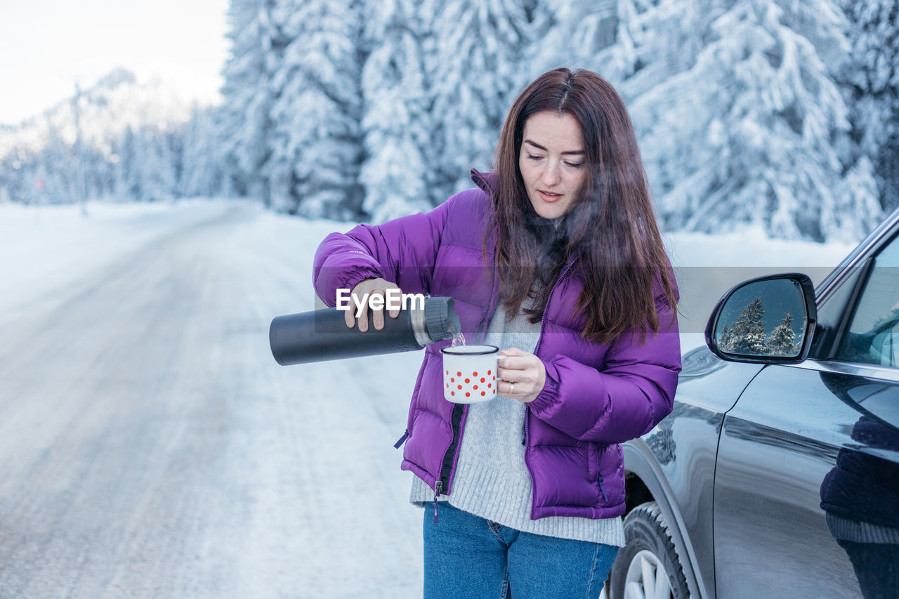 Woman drinking hot tea while on a road trip during winter.