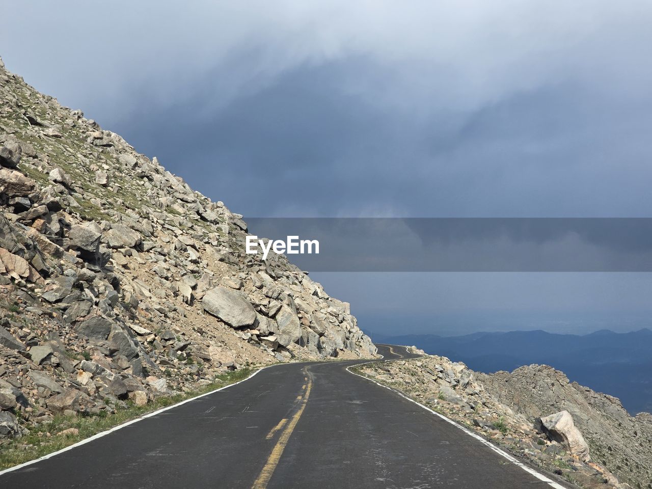 road, cloud, sky, transportation, mountain, environment, nature, landscape, the way forward, mountain range, scenics - nature, symbol, beauty in nature, mountain pass, no people, travel, travel destinations, land, outdoors, overcast, road marking, sign, day, vanishing point, non-urban scene, rock, marking, infrastructure, horizon, tranquility, ridge, dramatic sky, sea, empty road, highway, road trip, diminishing perspective, tranquil scene, tourism, street, asphalt, country road, remote, cloudscape, storm, architecture, fog