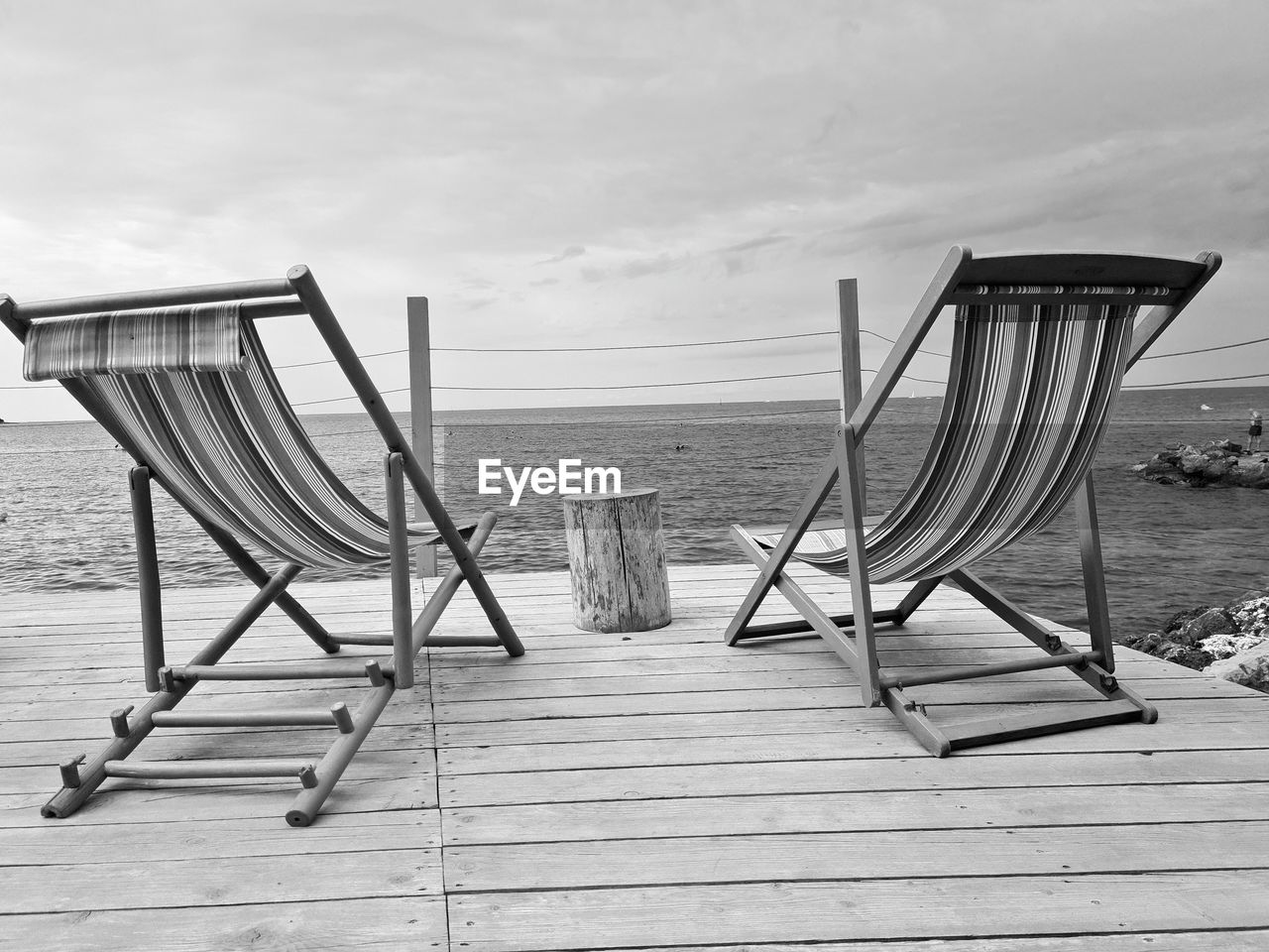 water, sky, beach, sea, land, chair, nature, black and white, tranquility, wood, seat, tranquil scene, cloud, beauty in nature, monochrome photography, scenics - nature, relaxation, absence, no people, sand, horizon, horizon over water, day, empty, holiday, monochrome, summer, white, deck chair, outdoors, sitting, vacation, trip, travel destinations, idyllic, pier, architecture, sunlight, furniture