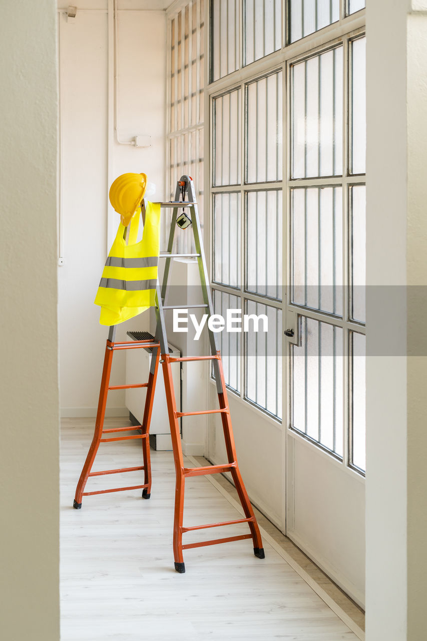 Hardhat and reflective waistcoat hanging on ladder in empty studio