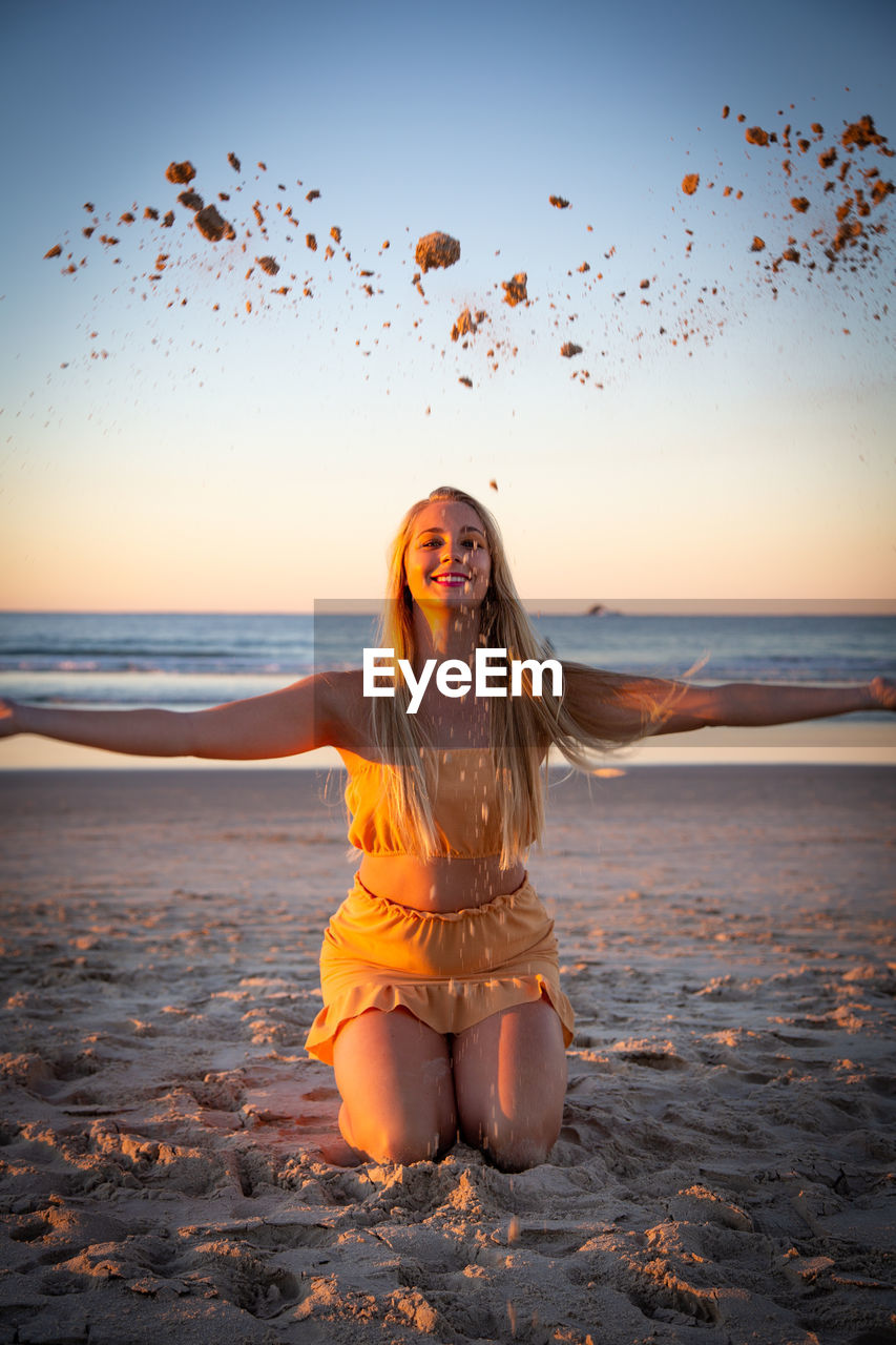 PORTRAIT OF YOUNG WOMAN AT BEACH DURING SUNSET