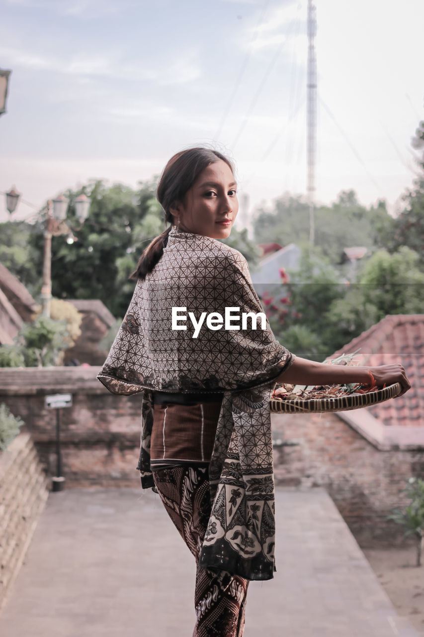 Portrait of young woman standing against sky