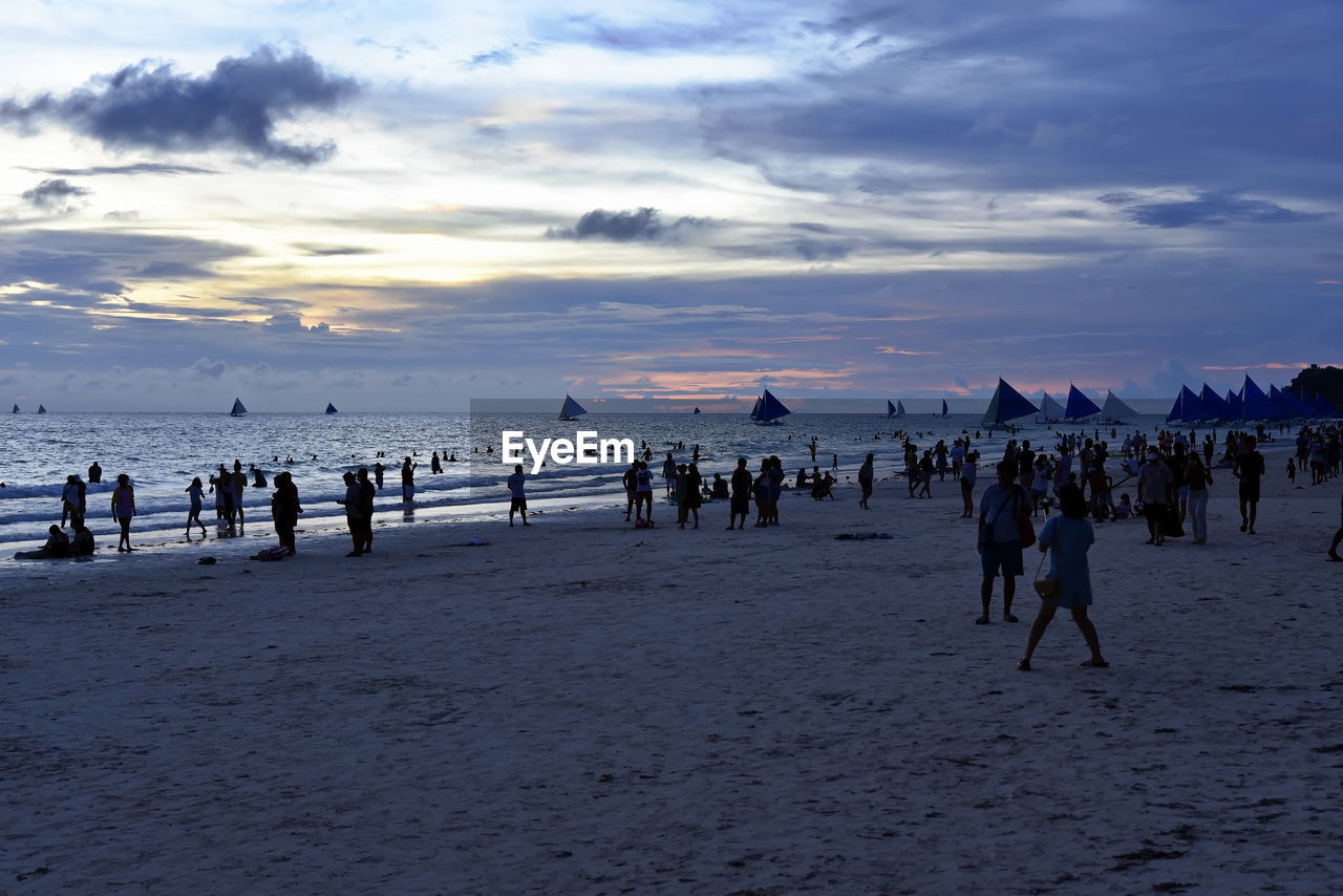 sky, beach, sea, land, water, large group of people, body of water, ocean, crowd, group of people, cloud, shore, nature, horizon, sand, sunset, coast, holiday, wave, vacation, trip, scenics - nature, beauty in nature, leisure activity, travel destinations, travel, dusk, evening, tourism, lifestyles, horizon over water, outdoors, silhouette, environment, men, enjoyment, tourist, landscape, women, winter