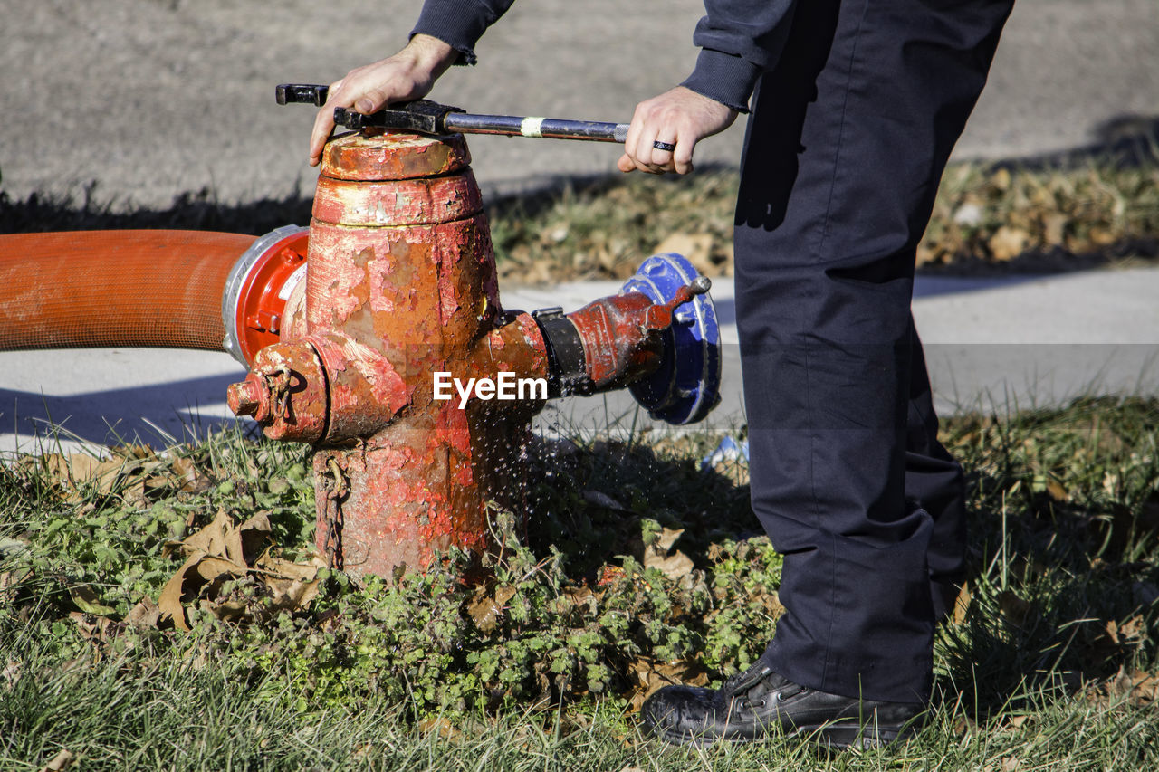 Low section of man adjusting water pipe while standing on grassy field