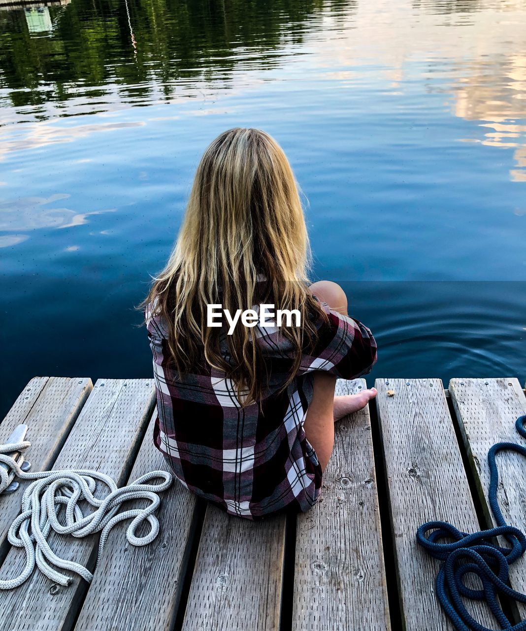 Rear view of woman sitting on jetty by lake