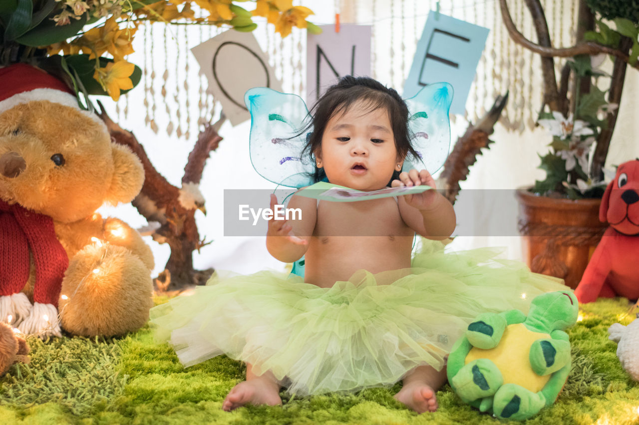 Cute shirtless baby girl sitting amidst stuffed toys during birthday