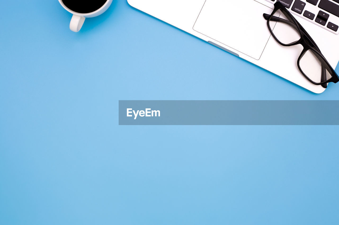 High angle view of eyeglasses over laptop by coffee cup against blue background