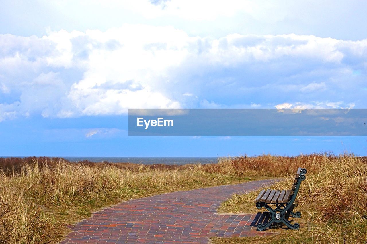 Park bench and seascape against sky