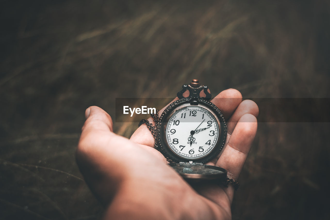 Cropped hand holding pocket watch outdoors