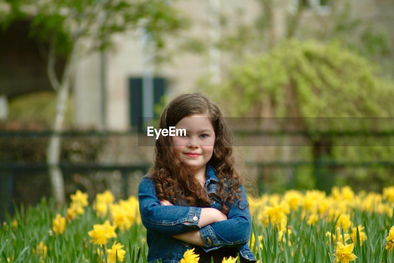 Portrait of girl standing with arms crossed amidst daffodils at park