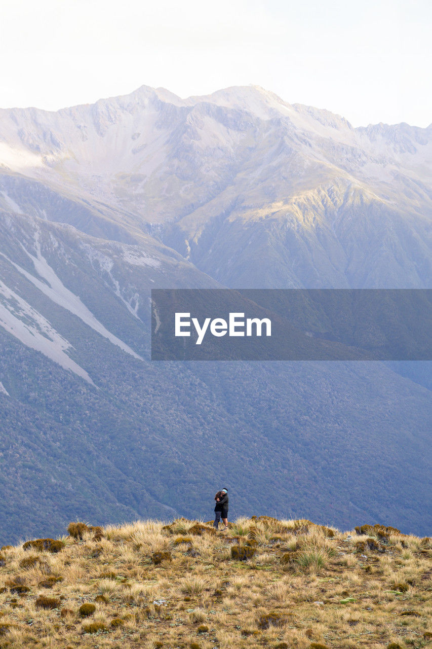 A couple embracing in front of mountains seen from the avalanche peak trail in arthur's pass