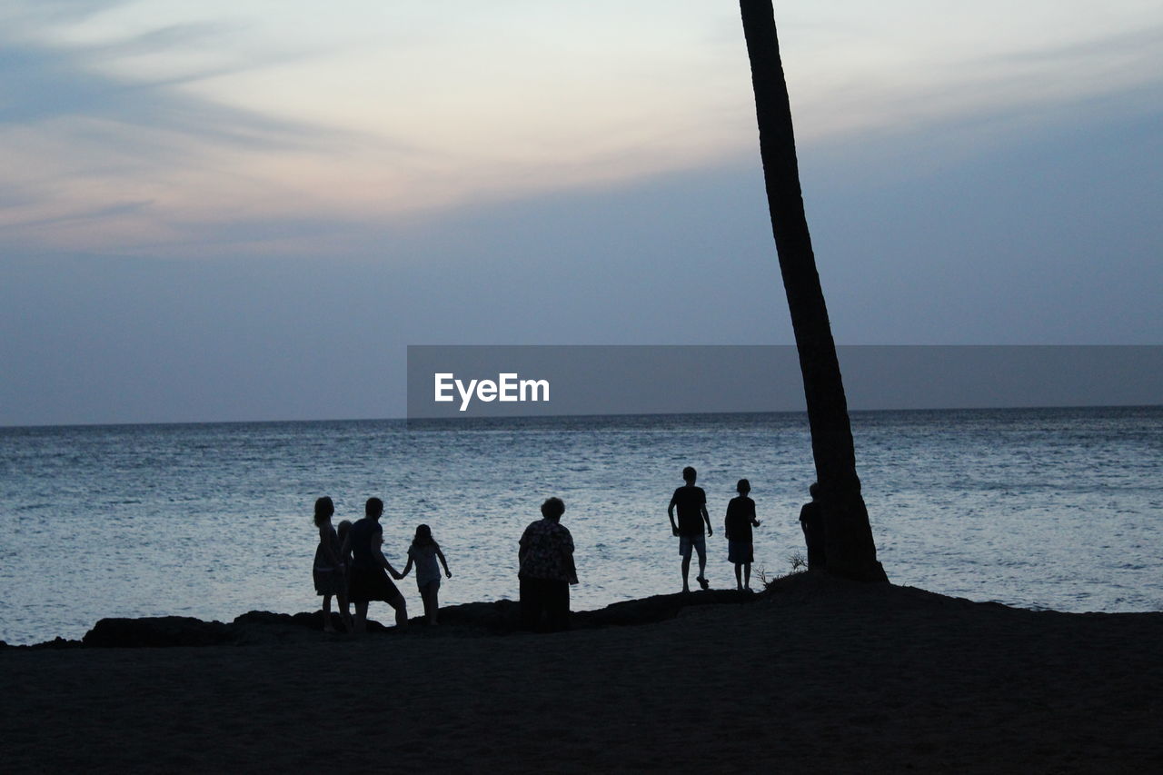 Silhouette people at beach against sky during sunset