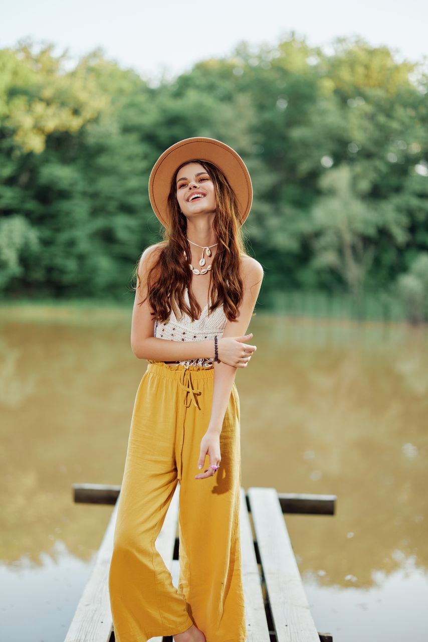portrait of young woman wearing hat while standing against lake