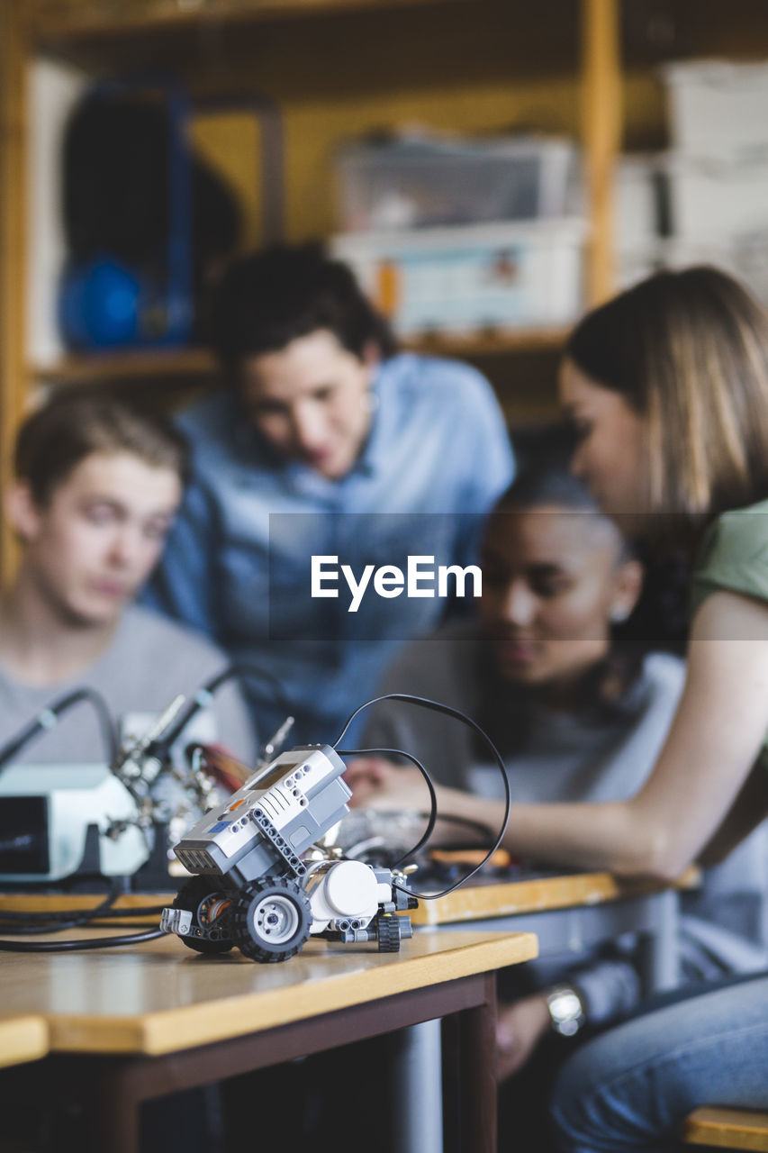 Toy car on desk against multi-ethnic students and teacher discussing in classroom at high school