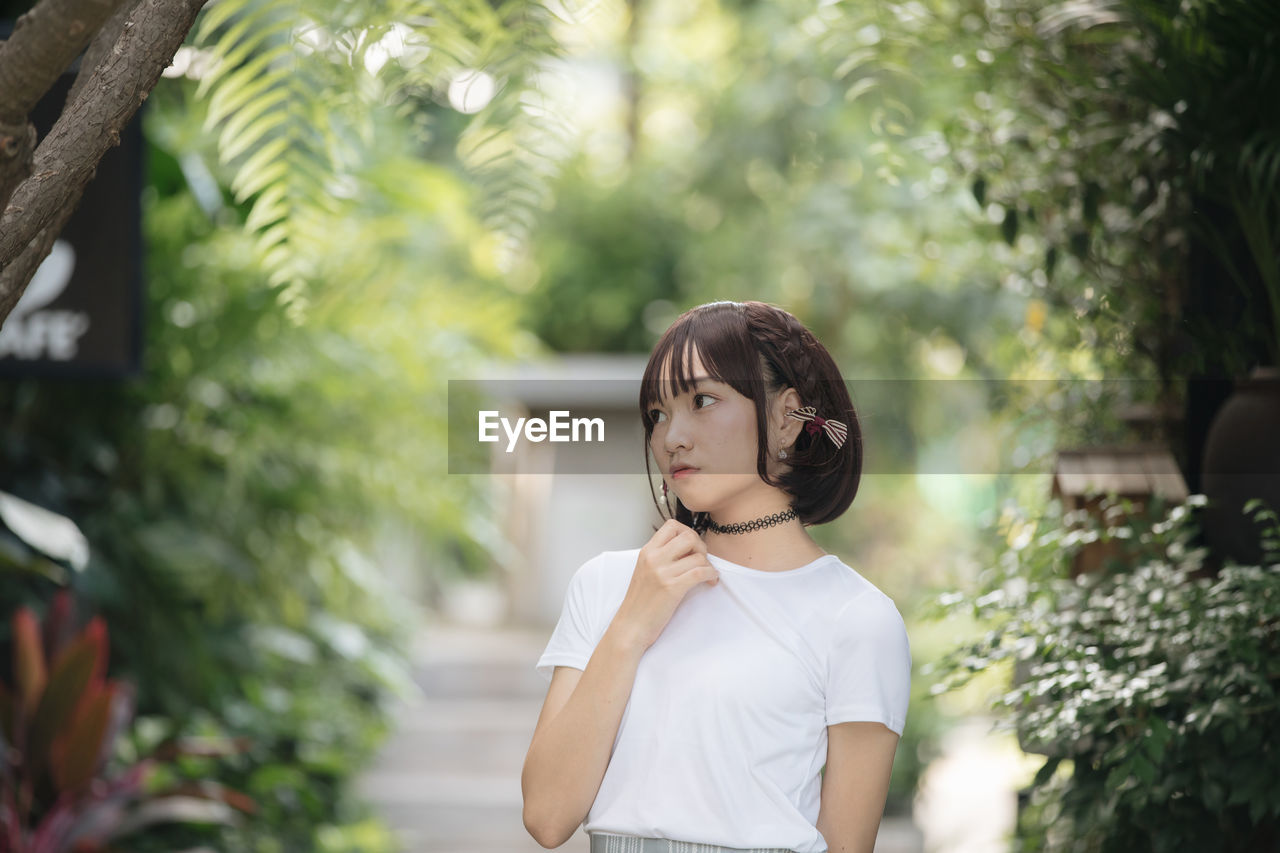 Young woman looking down while standing against trees