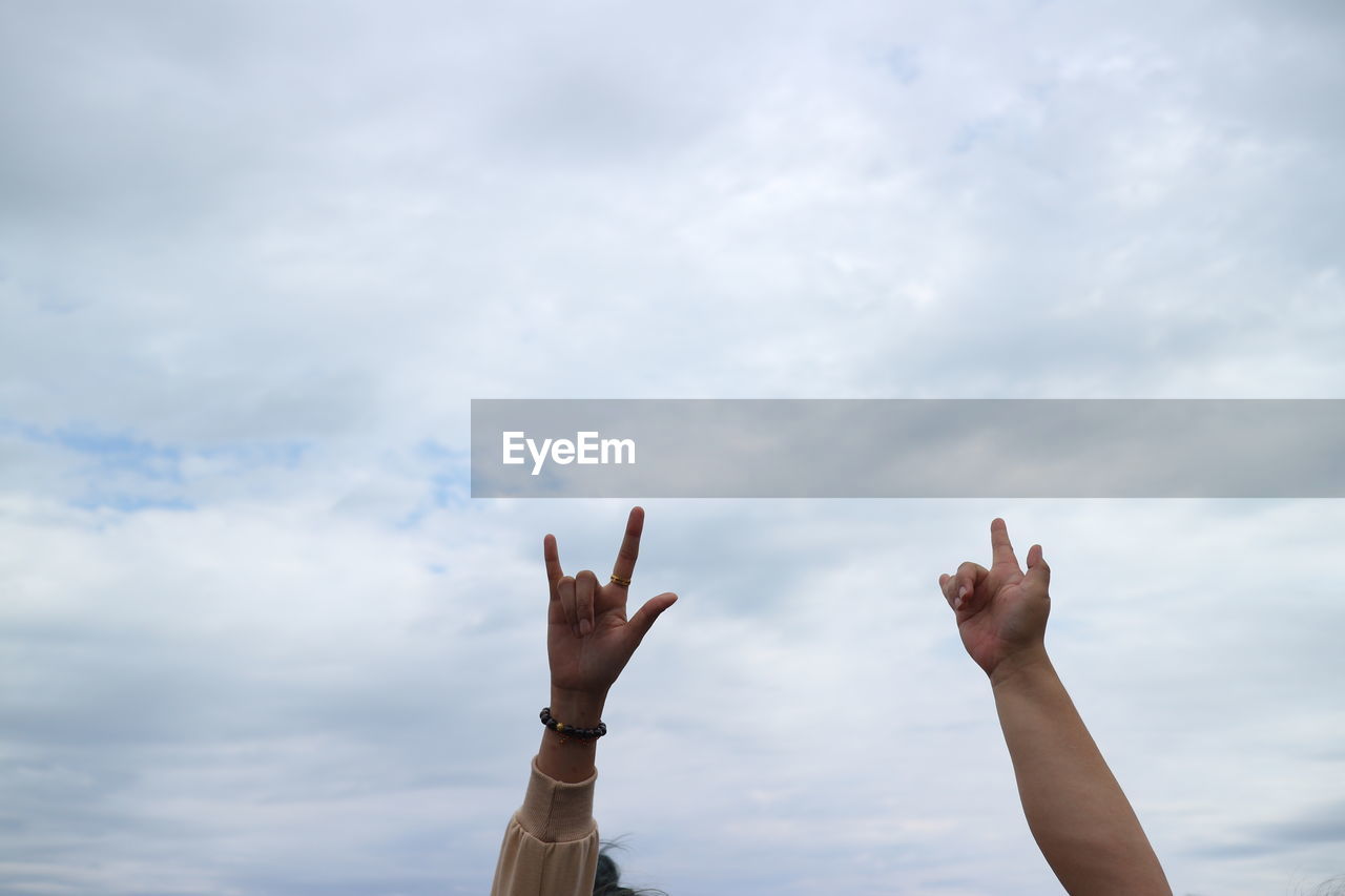 Cropped hand of people gesturing against sky