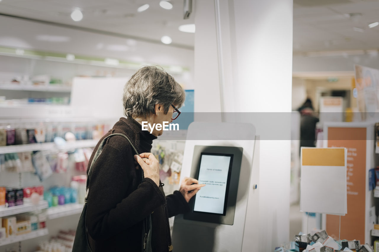 Side view of senior woman using kiosk at pharmacy store