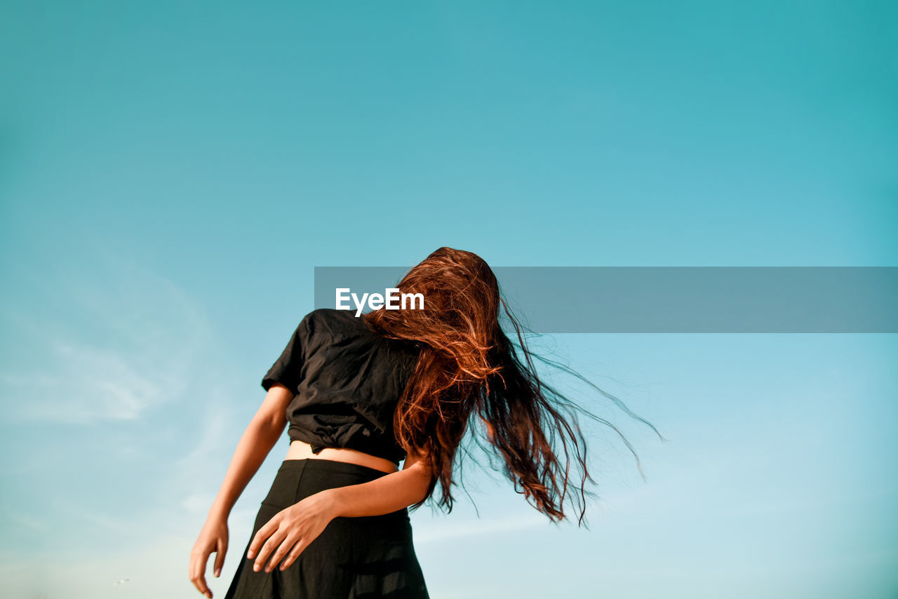 Low angle view of woman tossing hair against clear sky