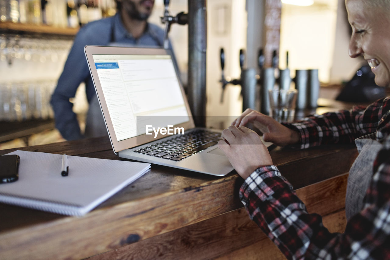 Smiling manager using laptop at bar counter