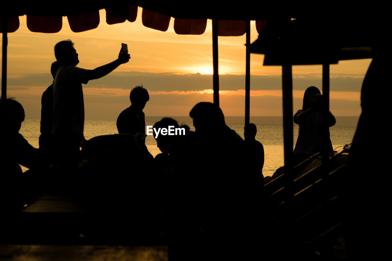 Silhouette people by sea against sky during sunset