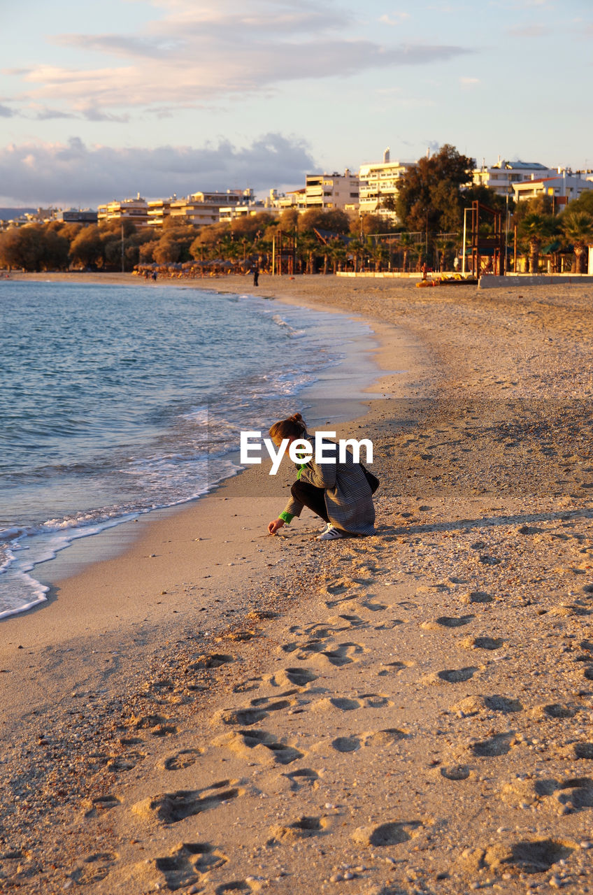 Woman sitting on beach against sky