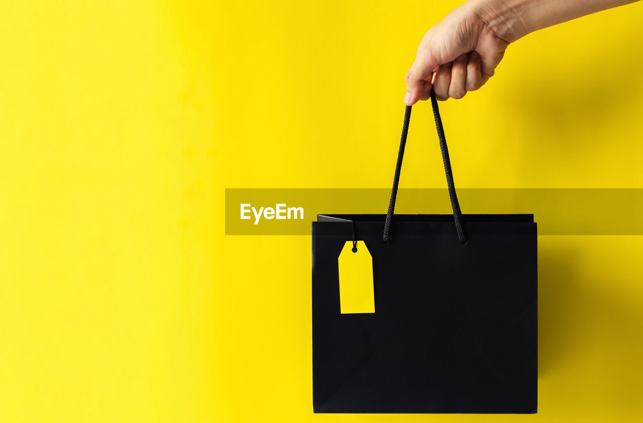 Hand holding black shopping bag with blank yellow price tag for black friday shopping sale concept.