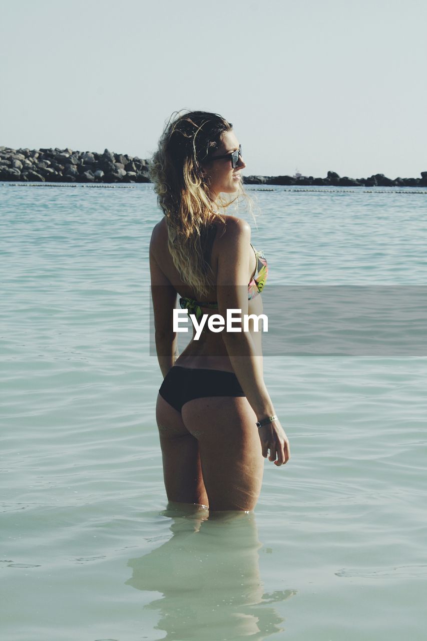 Rear view of beautiful woman in bikini standing in water