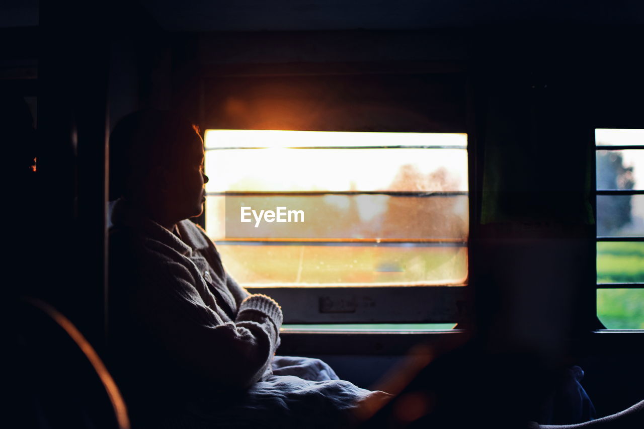 Side view of woman with arms crossed looking through window while traveling in train