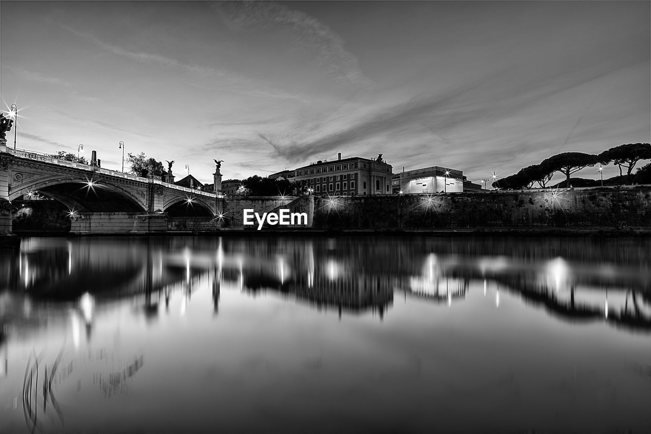 Bridge over river by buildings against sky in city