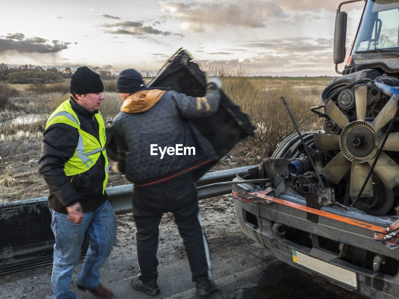 Mechanic with damaged truck on road during sunset