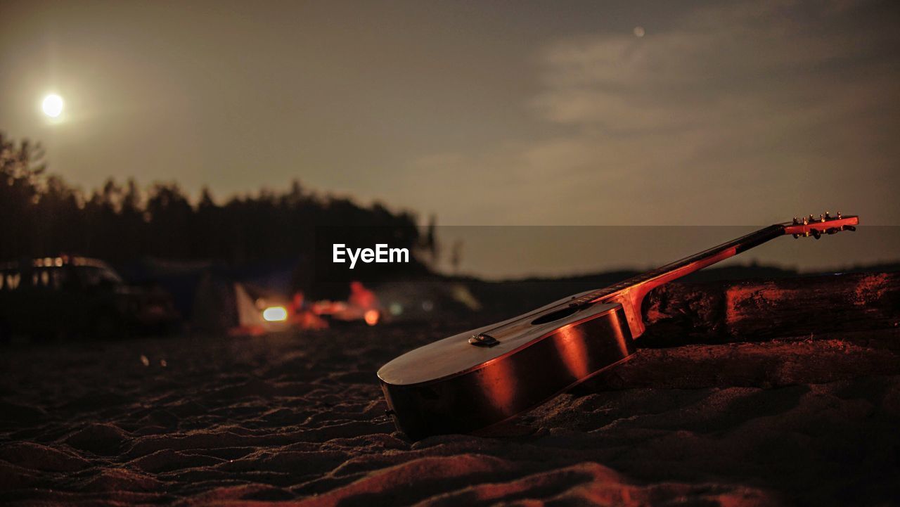 CLOSE-UP OF GUITAR AGAINST ILLUMINATED SKY DURING SUNSET