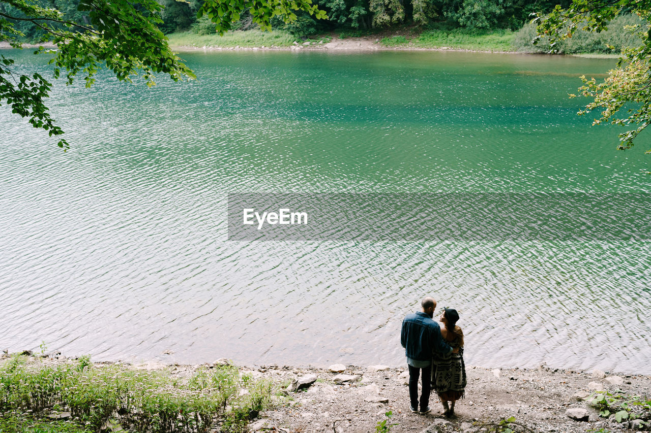 REAR VIEW OF MAN AND WOMAN WITH UMBRELLA ON LAKE