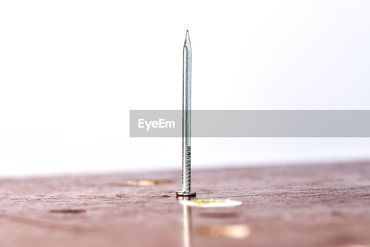 Close-up of nail on wooden table against white background