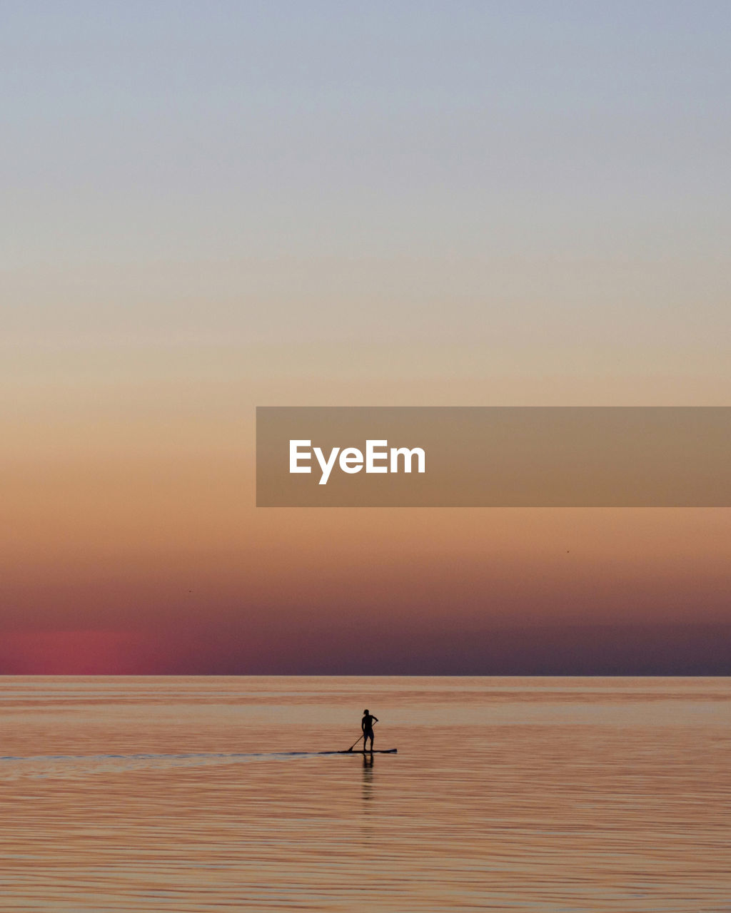 Silhouette person on the sup board on sea against sky during sunset. 