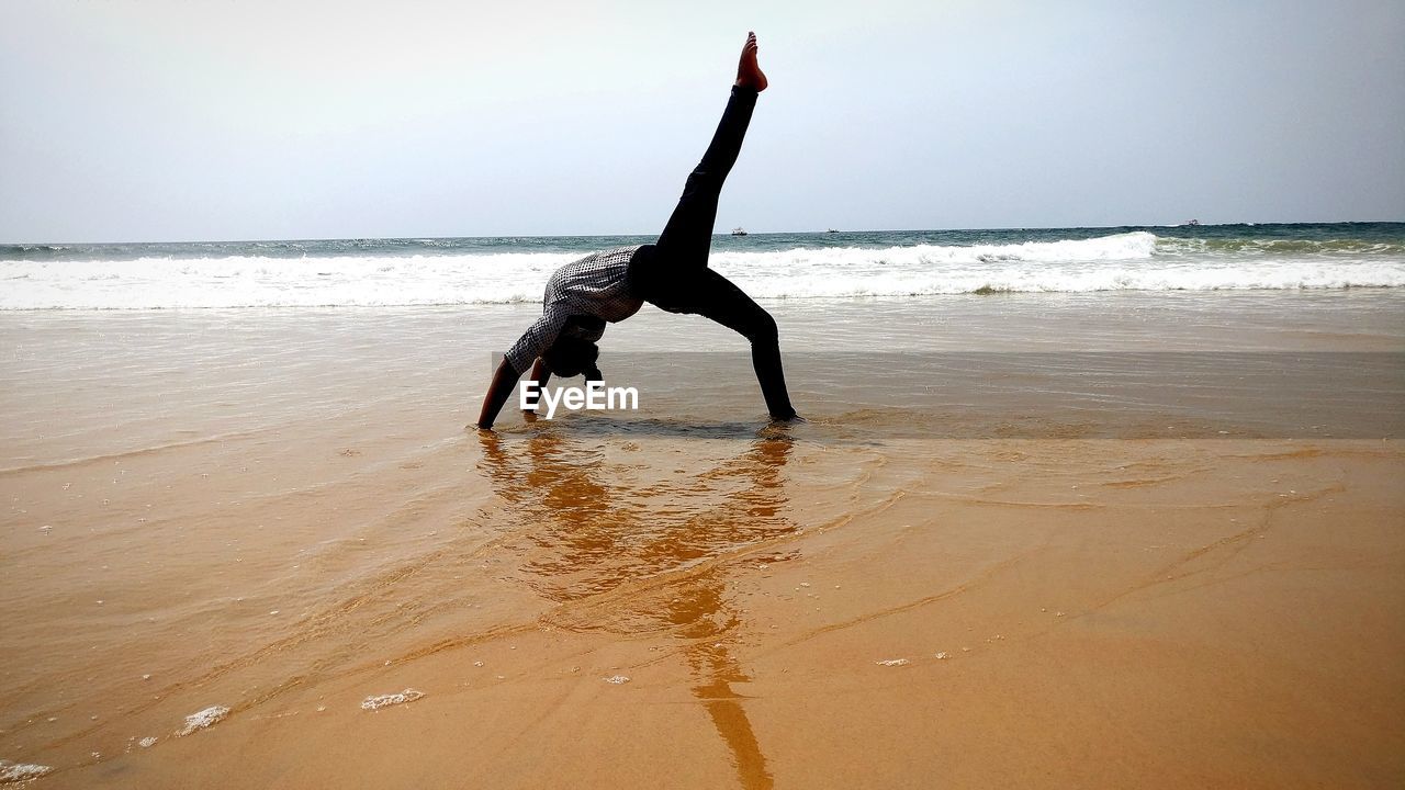 Woman doing stunt in sea against clear sky